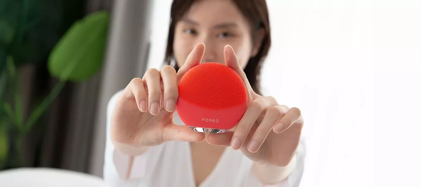 A young Asian woman showing of her LUNA facial cleansing brush